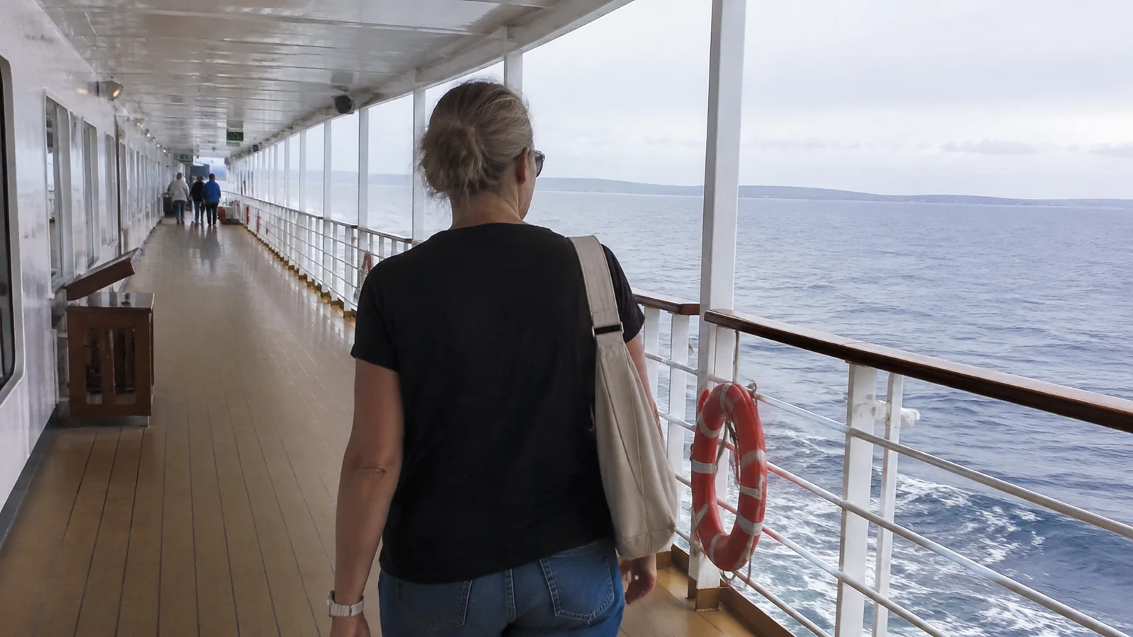 Woman walking along a sheltered ship promenade.