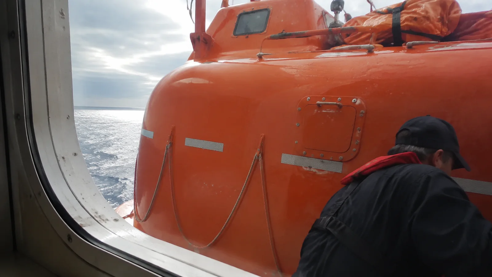 Orange lifeboat blocking much of the view through a cabin window.