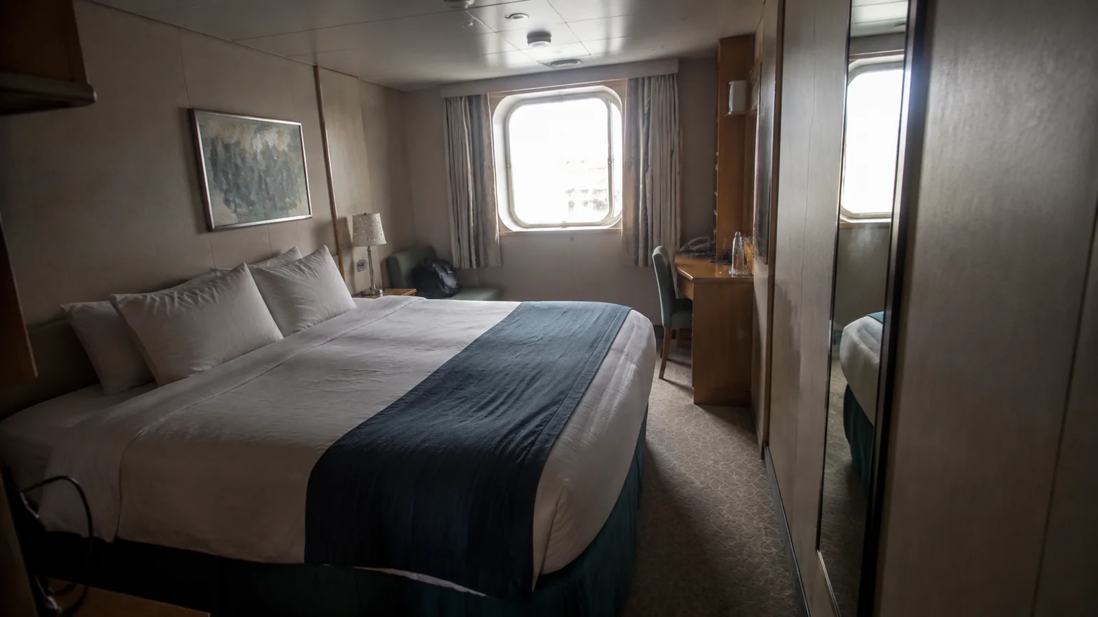 Cruise cabin with a double bed, desk, and narrow window