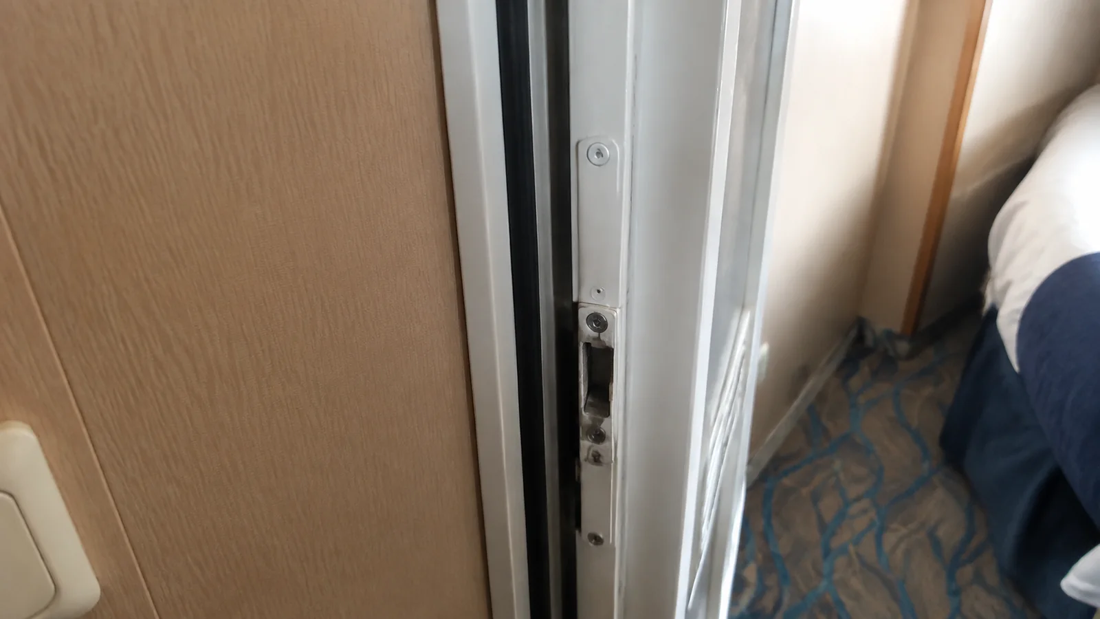 Close-up of a partially open connecting door beside a cruise cabin bed