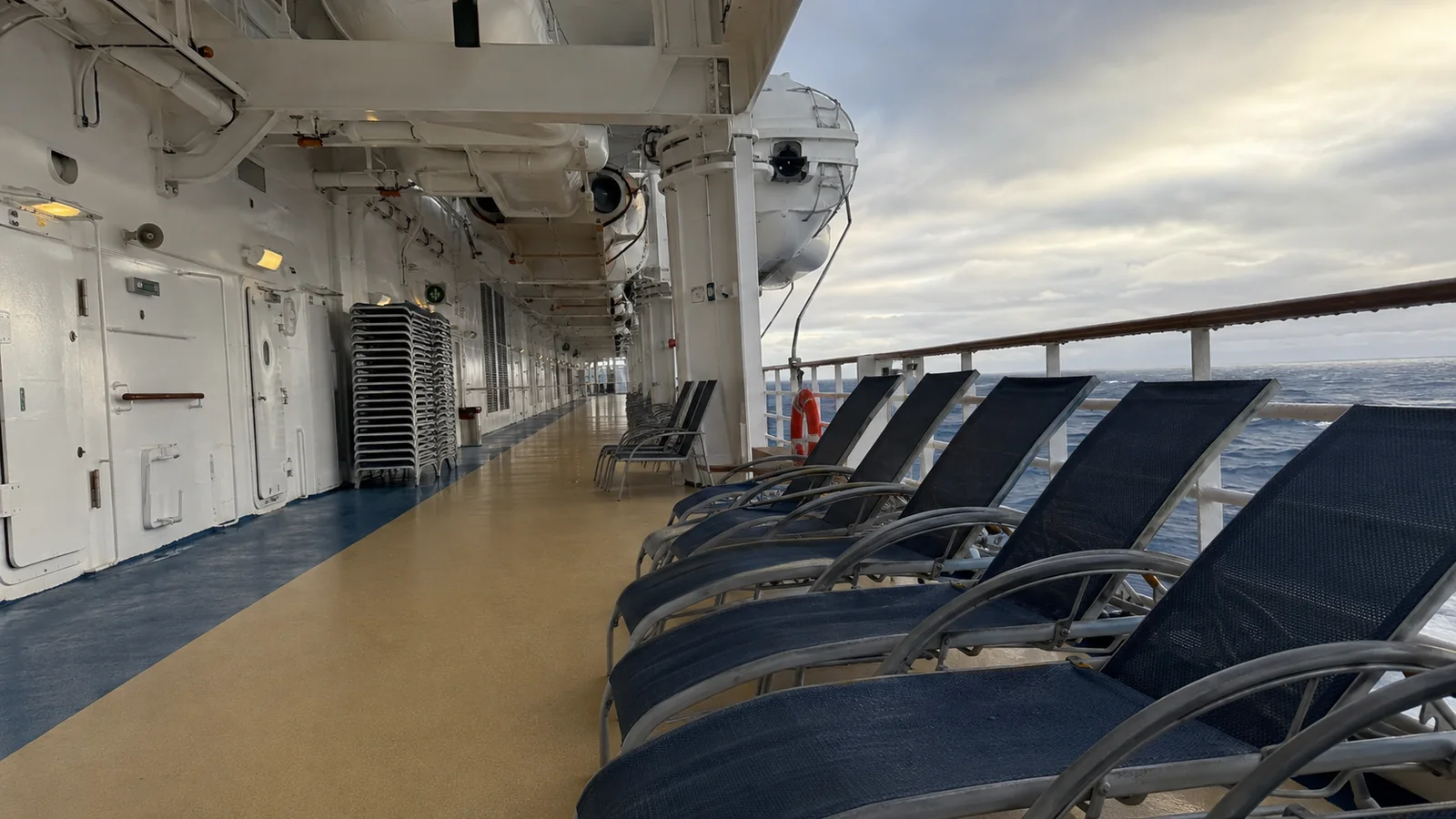 Empty blue lounge chairs along a covered cruise ship promenade