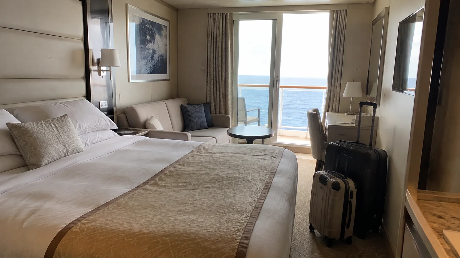 Balcony cabin with a large bed, sitting area and two suitcases.