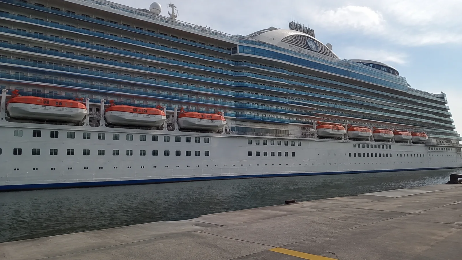 Cruise ship viewed from the quay with balcony decks above its lifeboats.