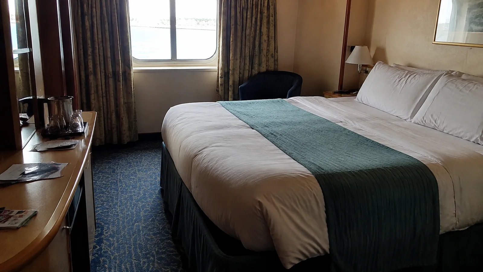 Cruise cabin with a double bed, desk, and curtained window