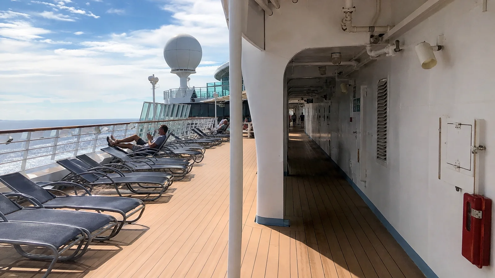 Sunlit cruise ship promenade with lounge chairs overlooking the ocean
