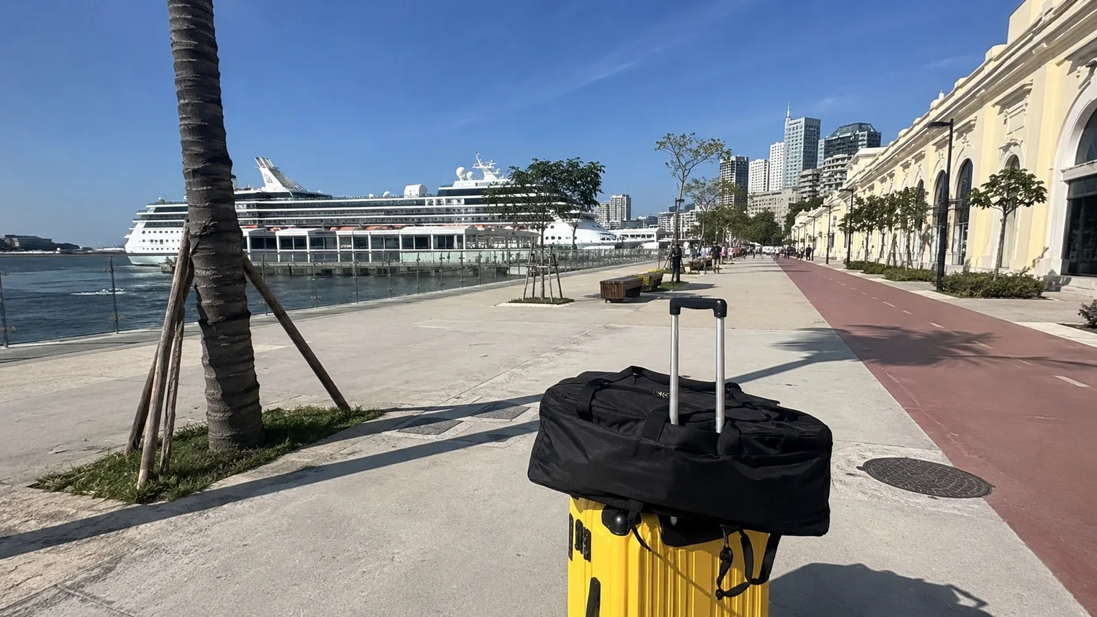 Yellow suitcase on a waterfront promenade with a cruise ship docked nearby