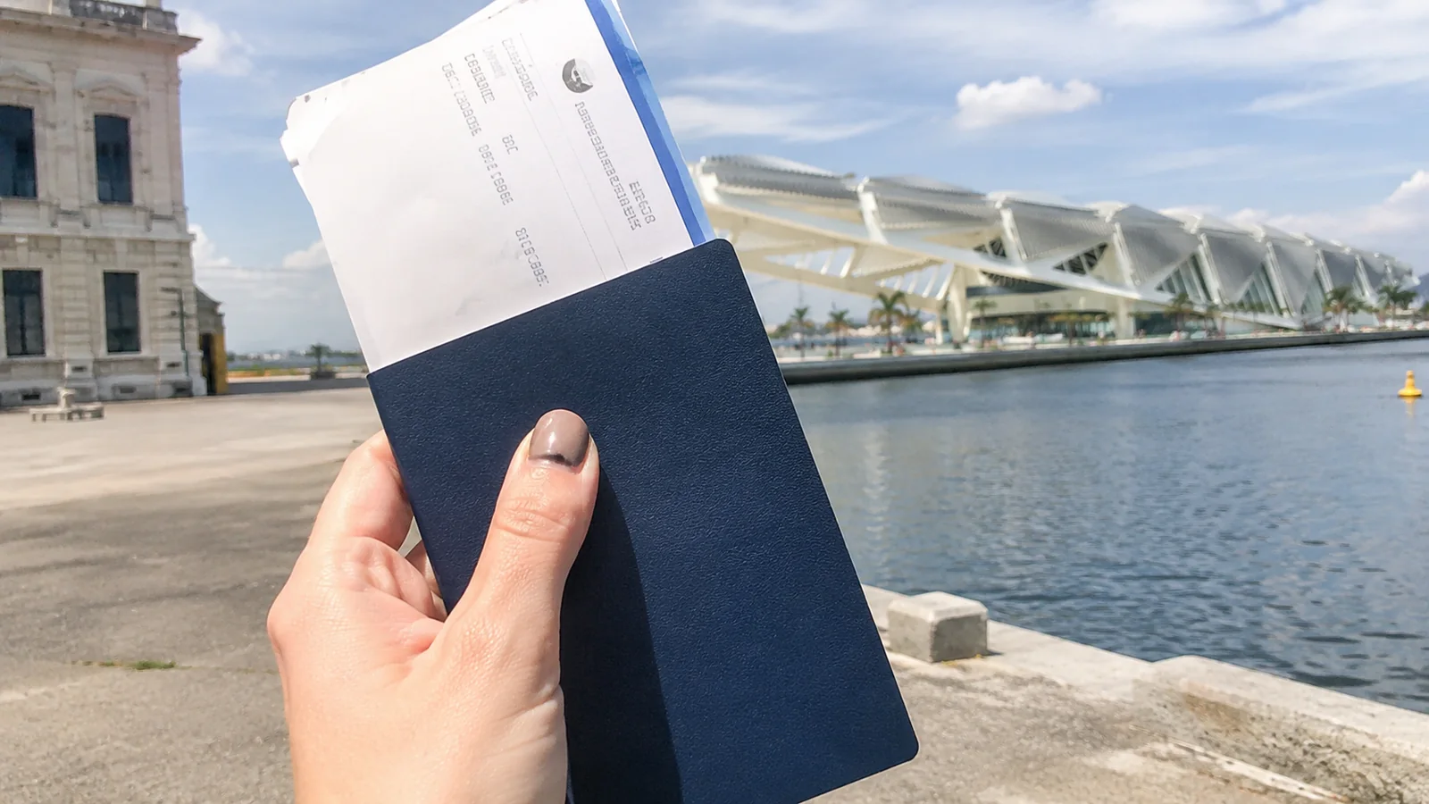 Hand holding a passport and boarding document at a waterfront cruise terminal