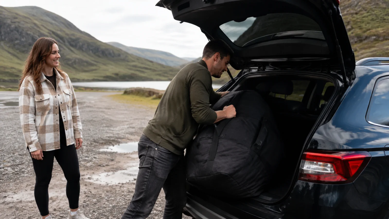 Traveler watches a companion rearrange luggage in a car's open trunk.