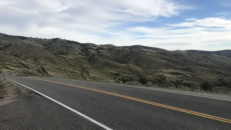 Paved road curves through open rocky hills beneath scattered clouds.