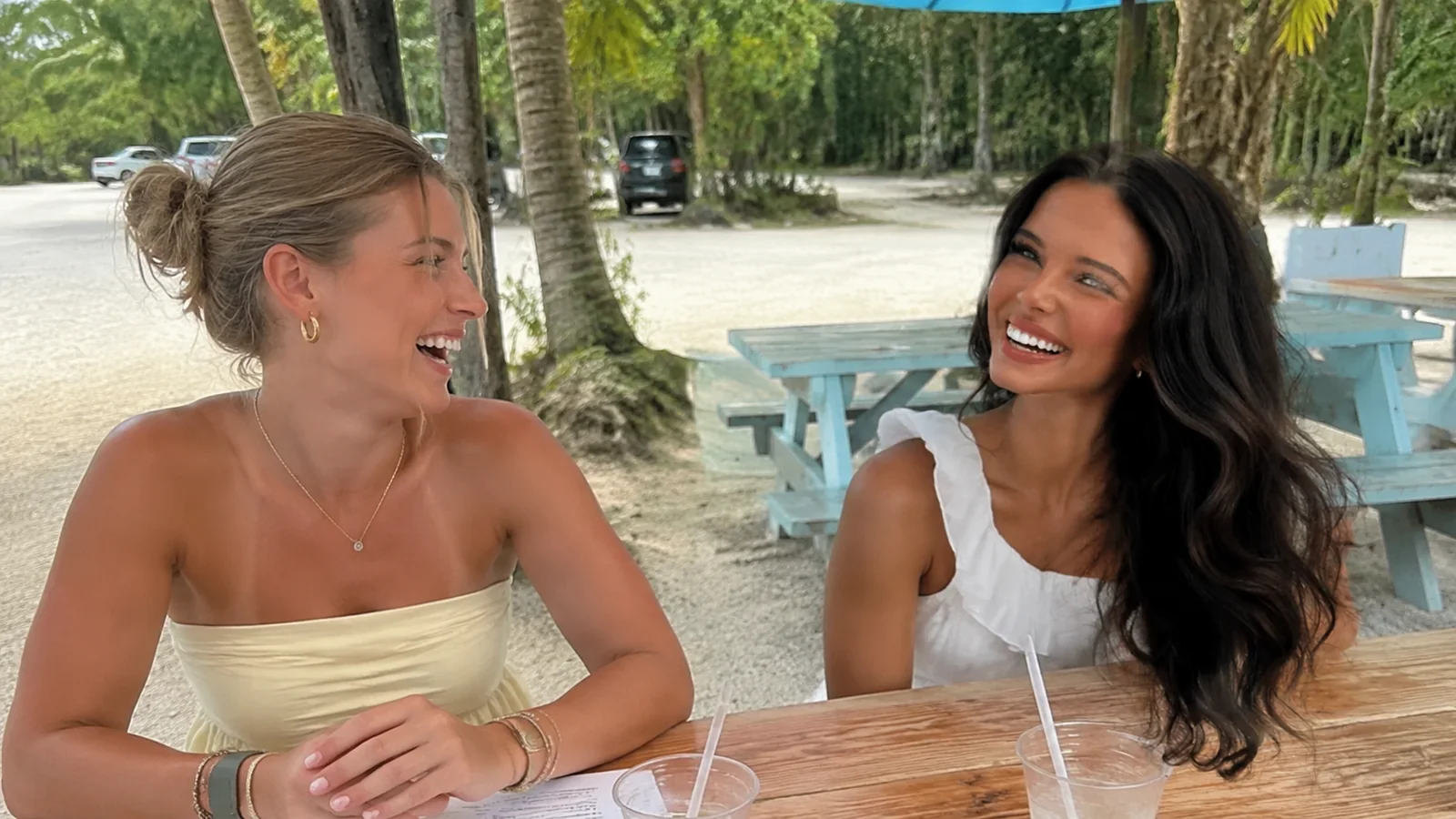 Two women laugh together at an outdoor picnic table.