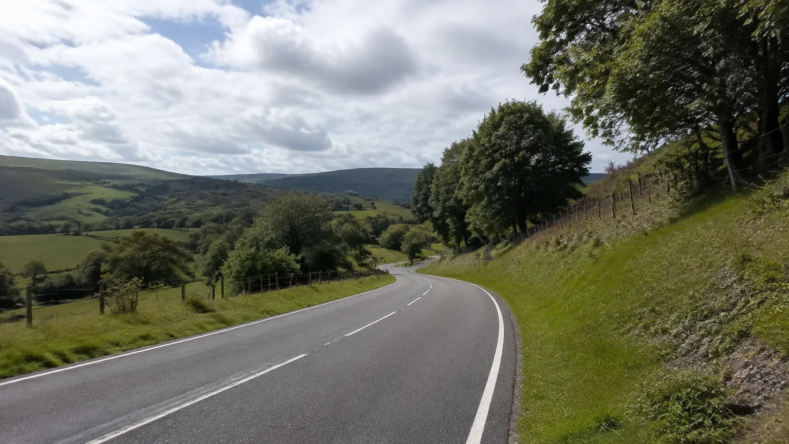 Empty road curves through green hills and scattered trees.