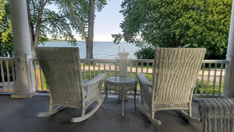 Two wicker chairs on a shaded porch overlooking a lake.