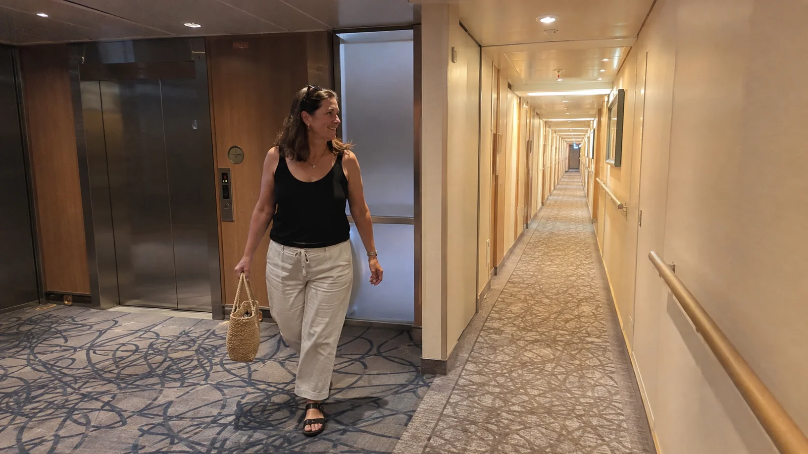 Woman walks past elevators into a long ship corridor.