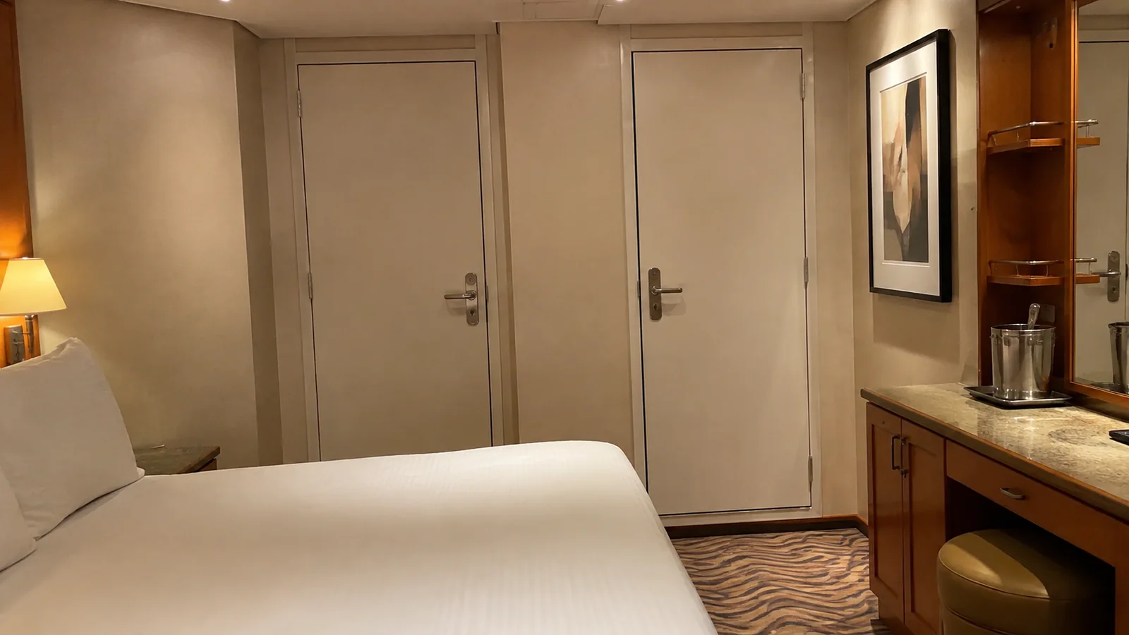 Two closed doors stand beside a stateroom bed and desk.
