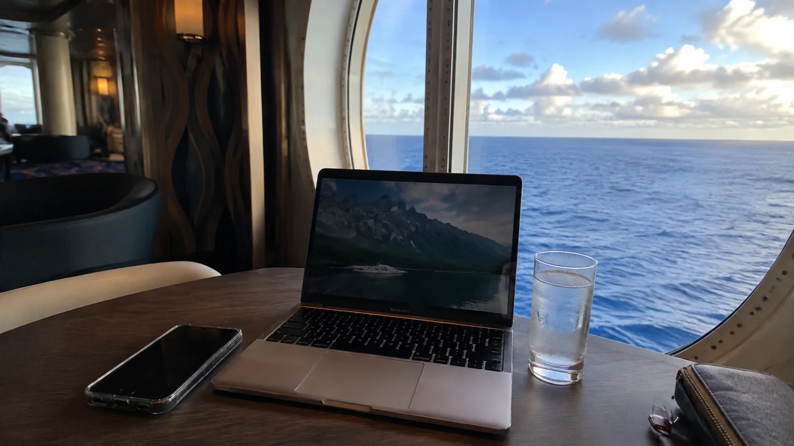 Laptop and smartphone on a lounge table beside an ocean-view window.