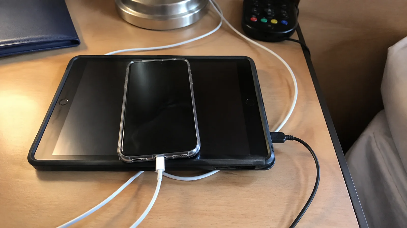 Tablet and smartphone connected to charging cables on a cabin desk.