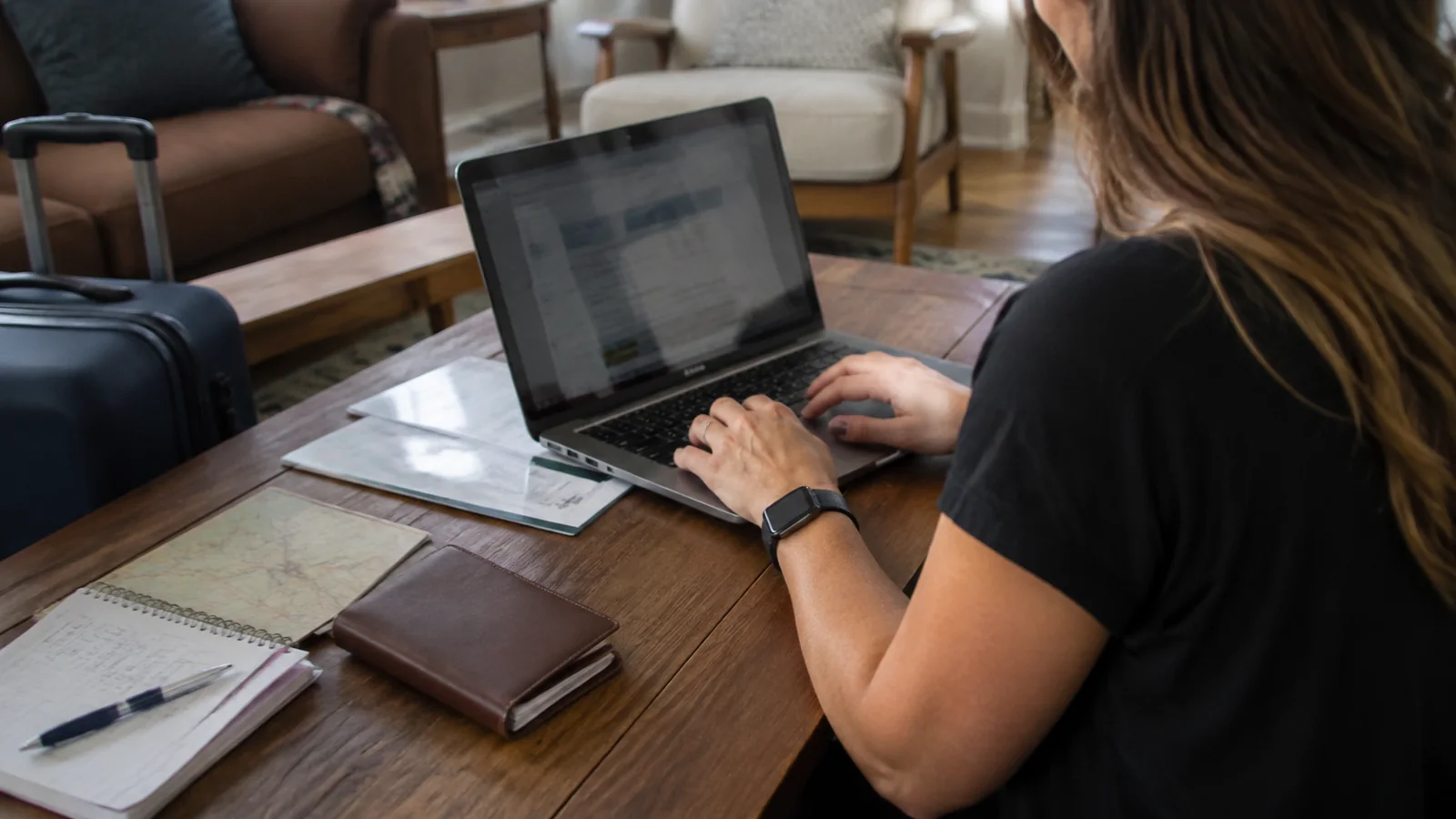 Traveler working on a laptop beside travel documents and a wallet.