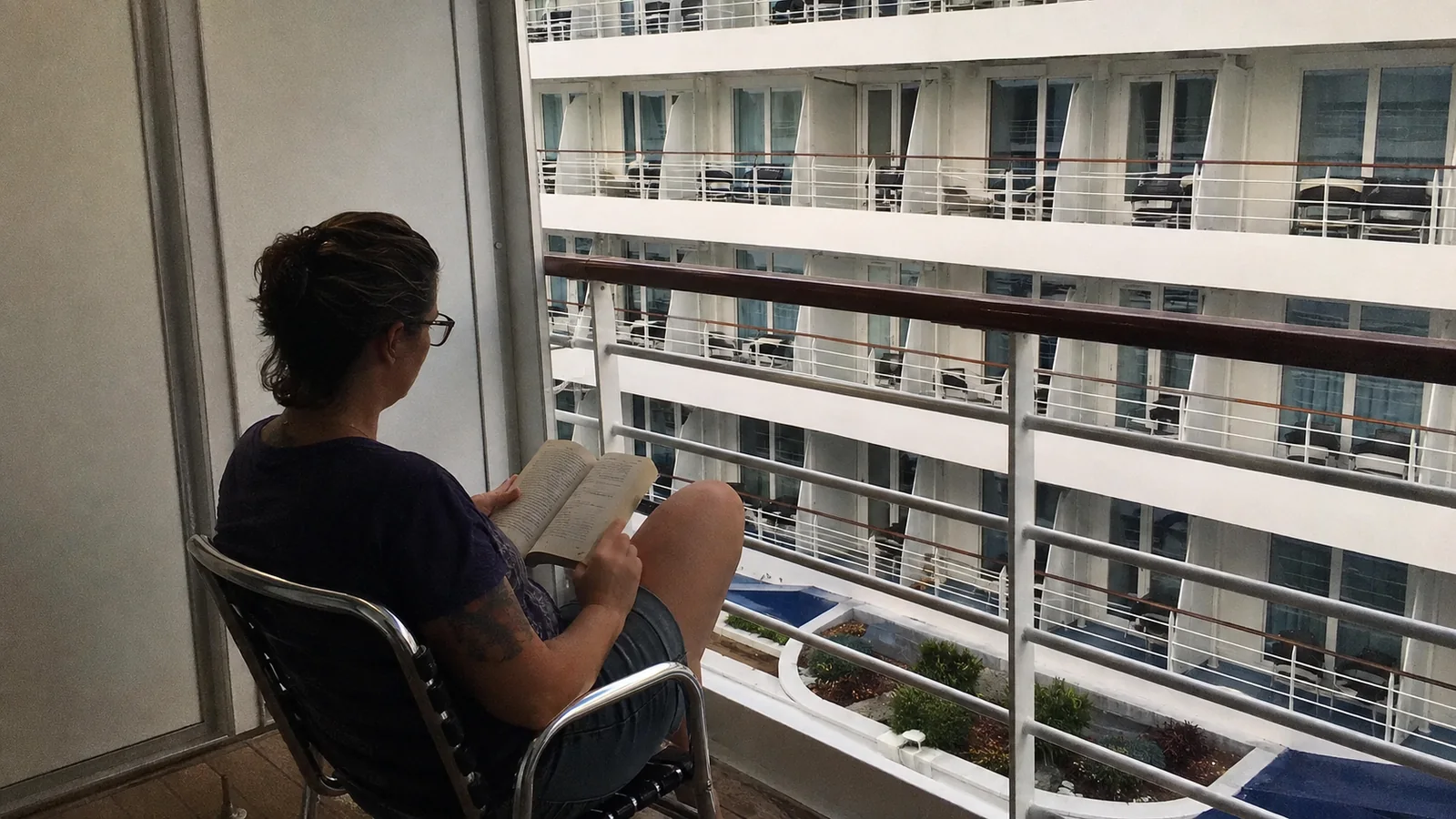 Passenger reads on a balcony facing rows of opposite balconies.