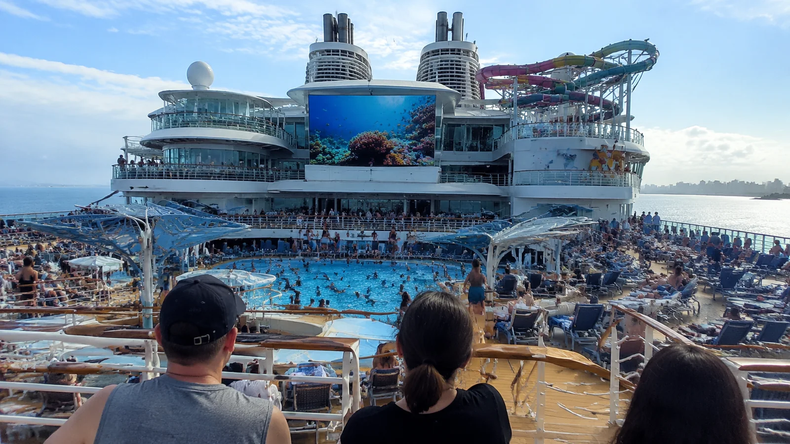 Passengers overlooking a crowded cruise ship pool and water-park deck