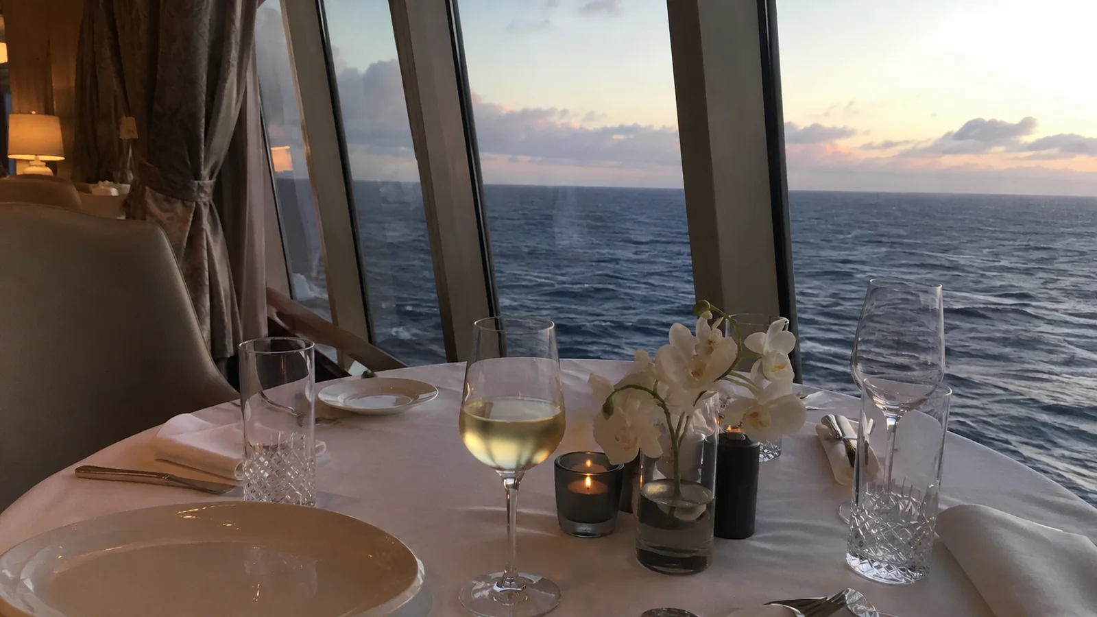Table settings and flowers stand beside windows overlooking the sea.