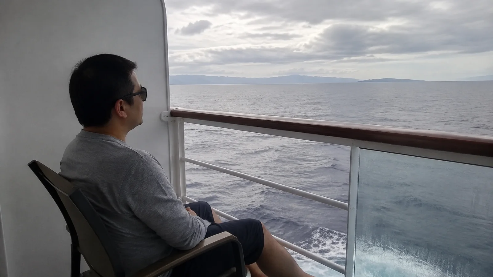 Man sits on a balcony chair looking over the sea.