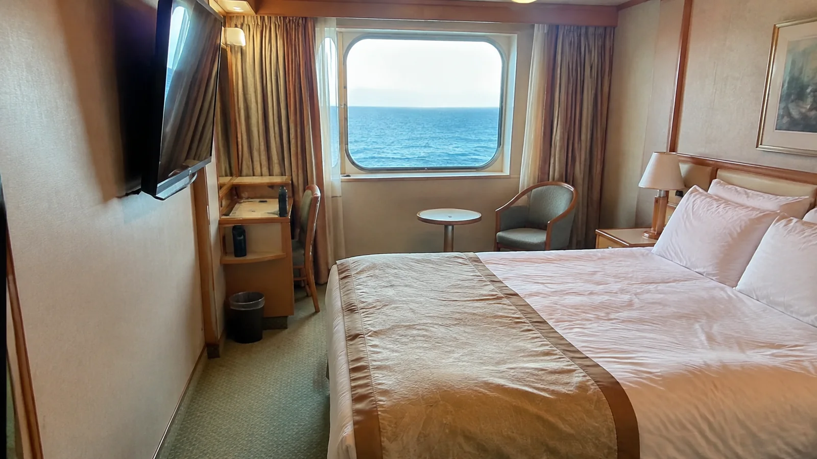 Cruise cabin with a double bed and chairs beside an ocean-view window