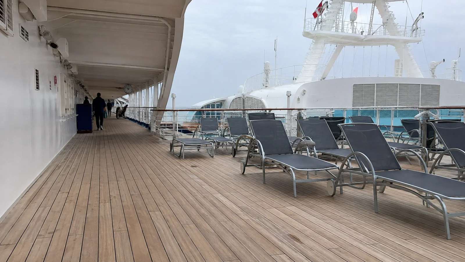 Lounge chairs on a wooden cruise ship deck beneath an overhang