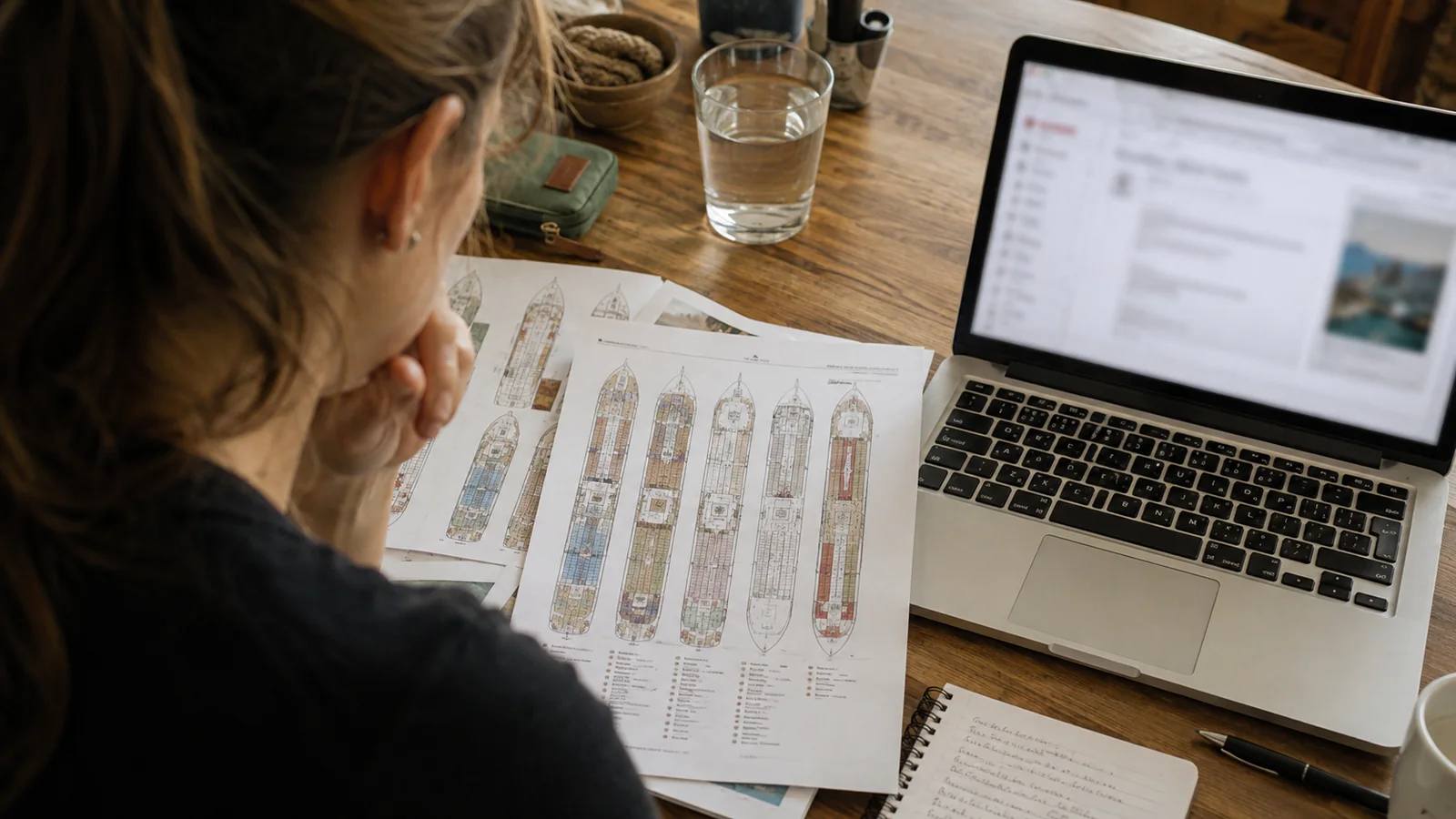 Woman reviewing printed cruise ship deck plans beside a laptop