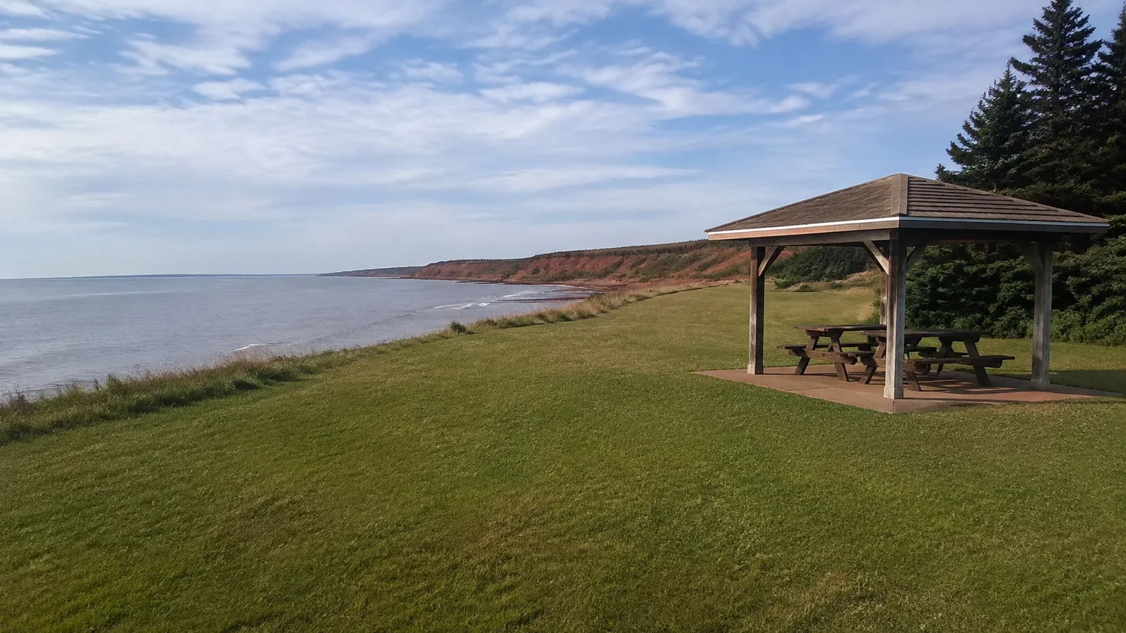 Small picnic shelter on a grassy slope overlooking the sea.