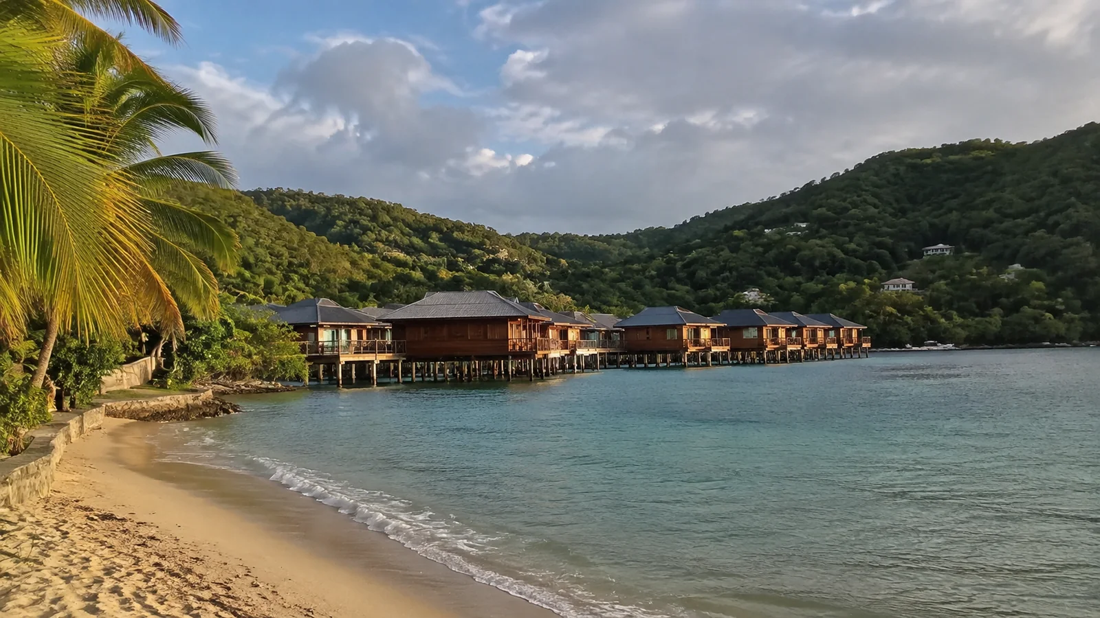 Beach and overwater villas beneath a green hillside.