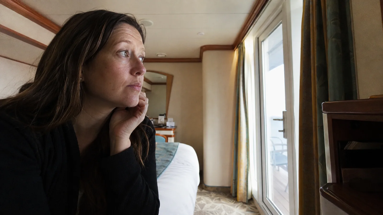 Passenger looking through a cabin window beside the bed.