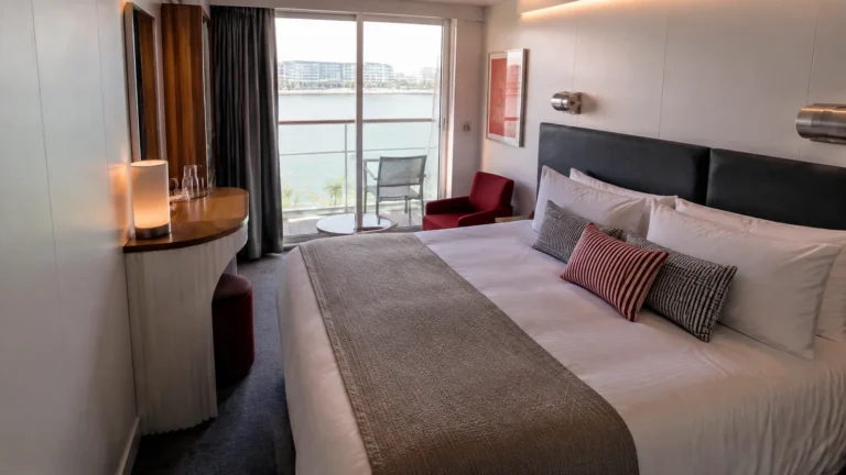 Modern stateroom has a double bed and glass balcony doors.