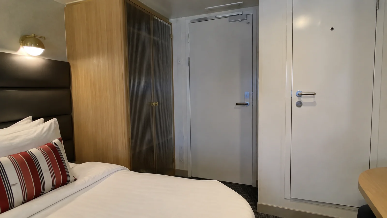 Closed doors stand beside a bed with a dark padded headboard.