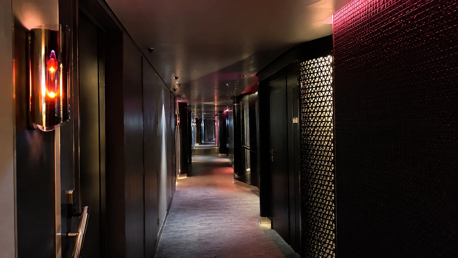 Dim corridor has decorative wall lights and closed dark doors.