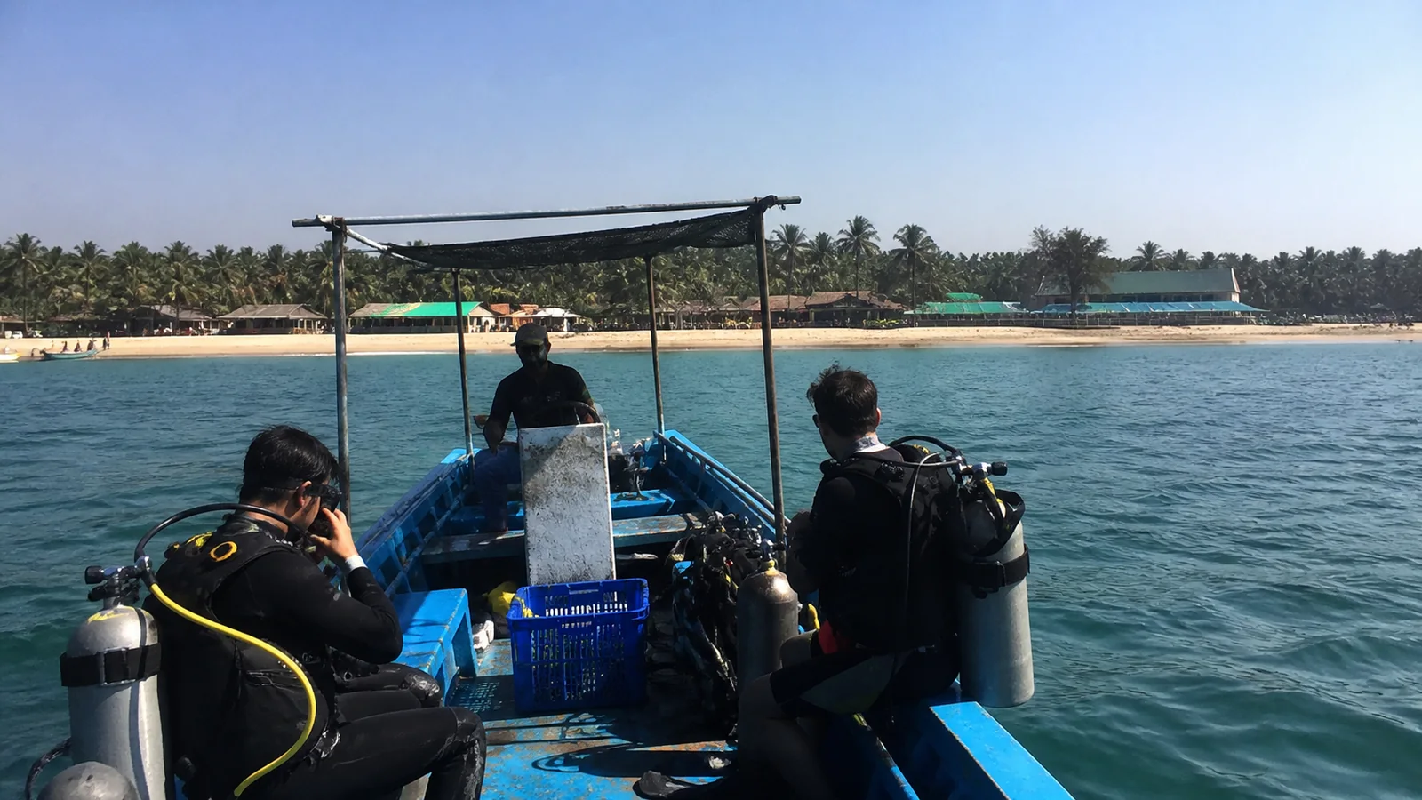 Divers preparing equipment in a small boat near a palm-lined beach.