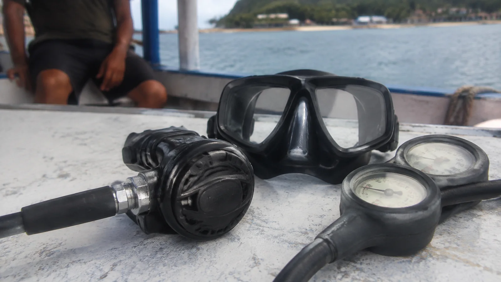 Scuba mask, regulator and pressure gauges on a boat bench.