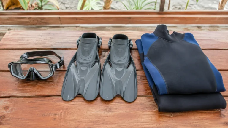 Diving mask, fins, and folded wetsuit arranged on a wooden surface.