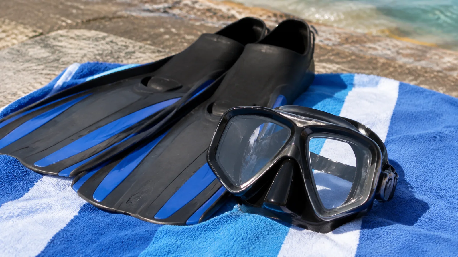 Blue-and-black fins and diving mask resting on a striped towel.