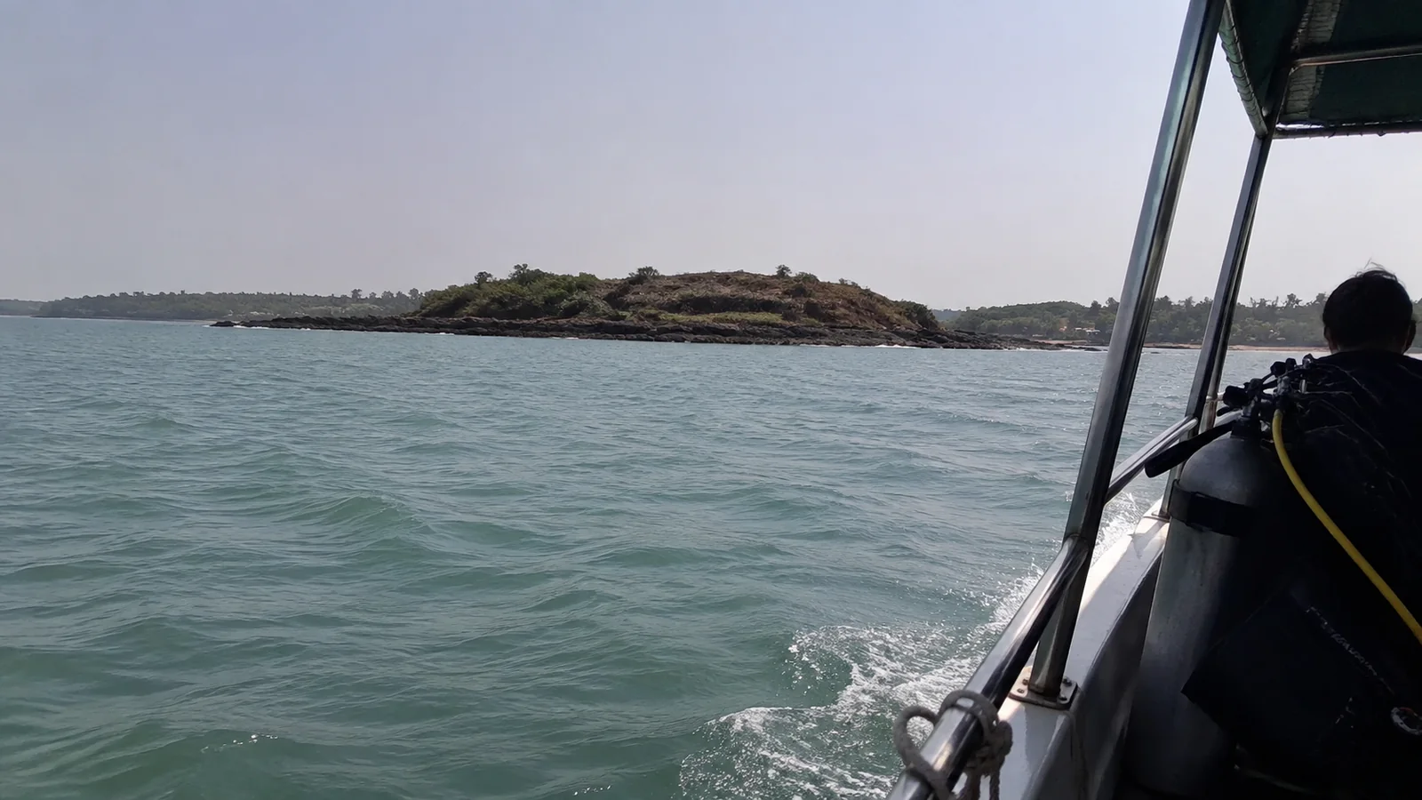 Boat approaching a low rocky island across green-gray water.