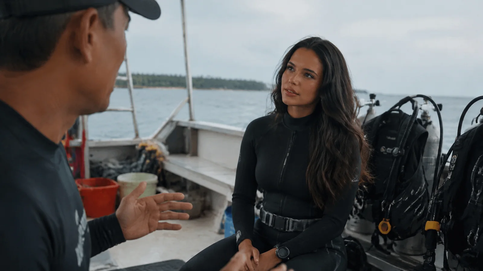 Diver listening to a briefing aboard a boat with scuba tanks nearby.