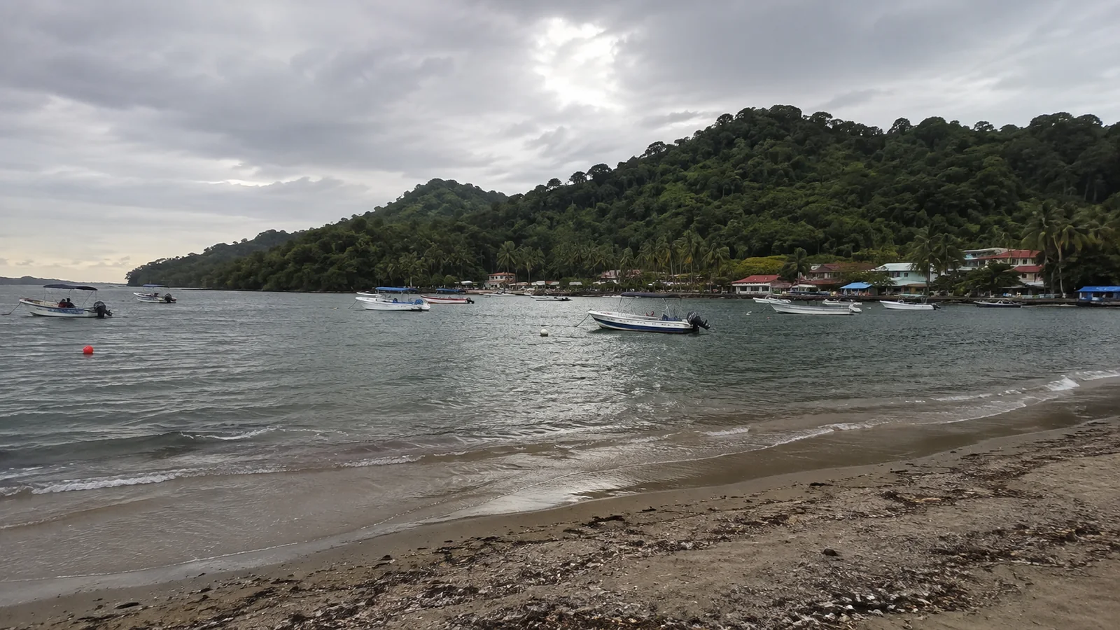 Small boats anchored in a sheltered bay below a forested hill.