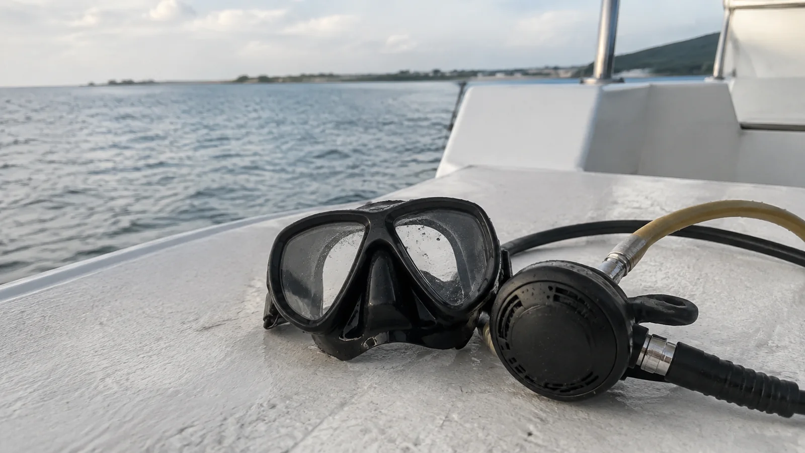 Diving mask and regulator rest on a boat ledge beside the water.