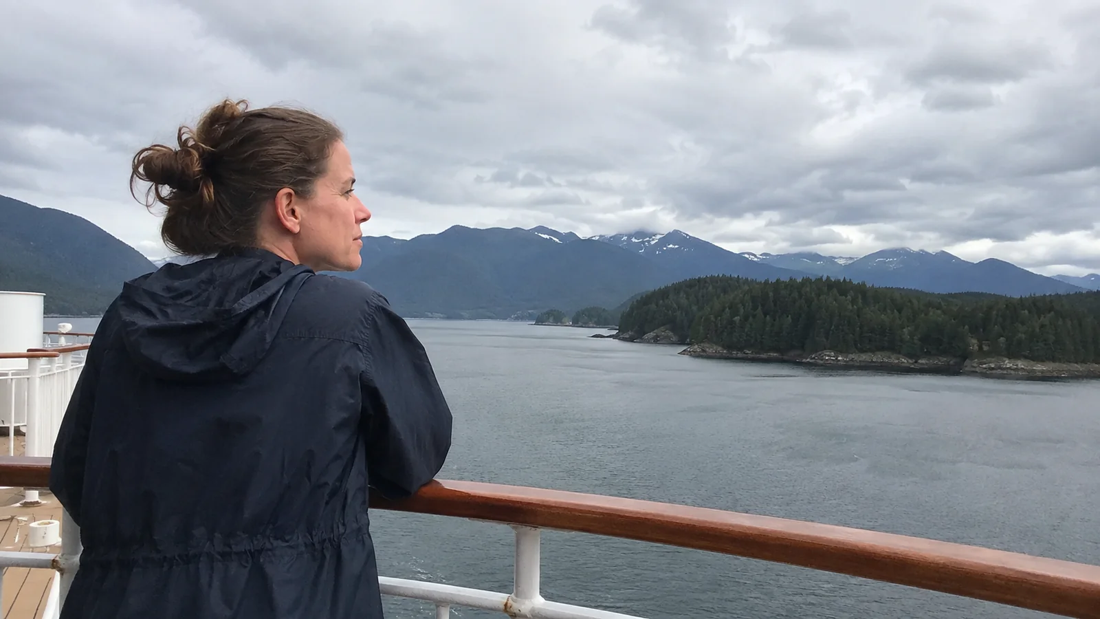 Passenger looks across forested islands and mountains from a ship's railing.