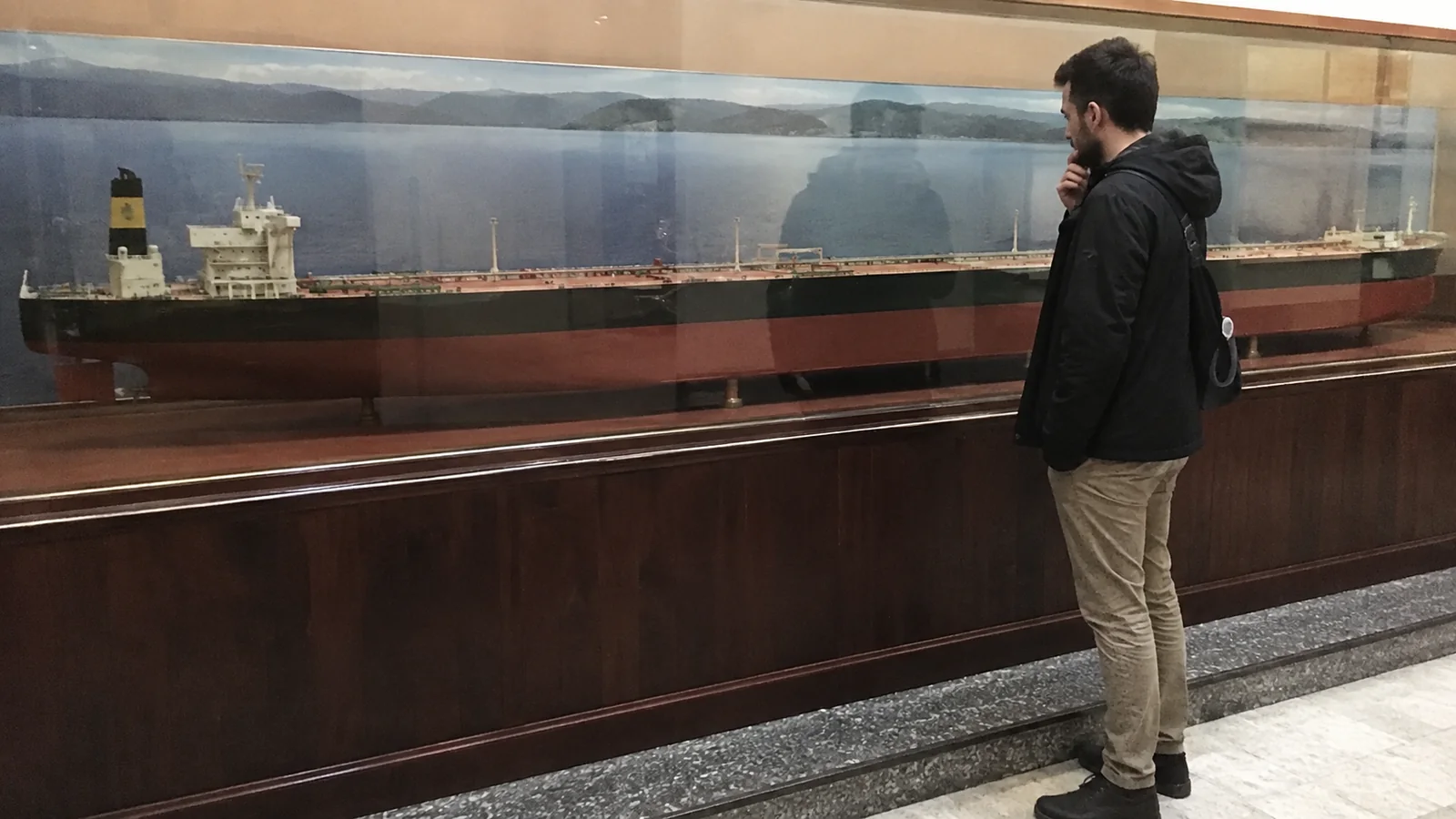 Visitor viewing a large tanker model in a glass case.