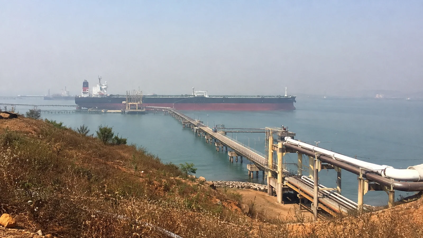 Oil tanker moored at the end of a long offshore loading pier.