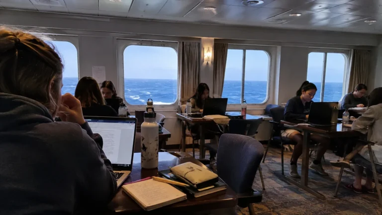 Students working on laptops in a shipboard classroom.