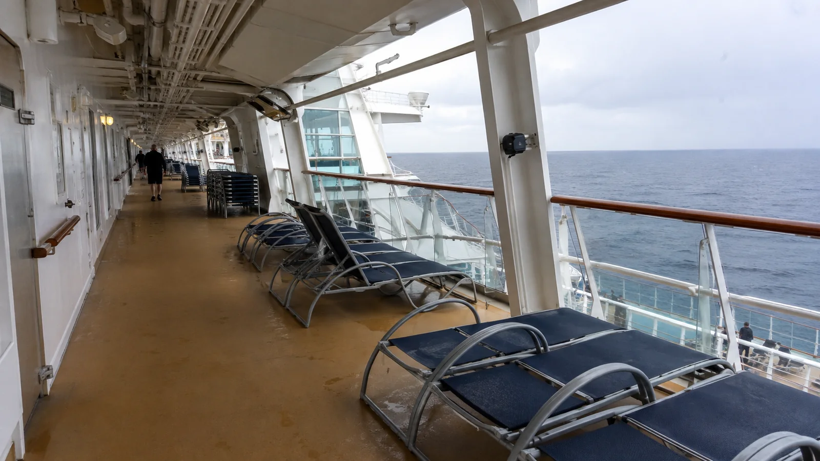 Empty lounge chairs on a covered cruise ship promenade overlooking the ocean