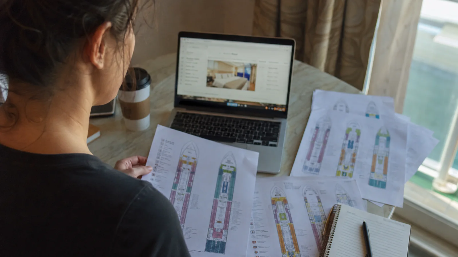 Woman holding printed cruise ship deck plans beside a laptop