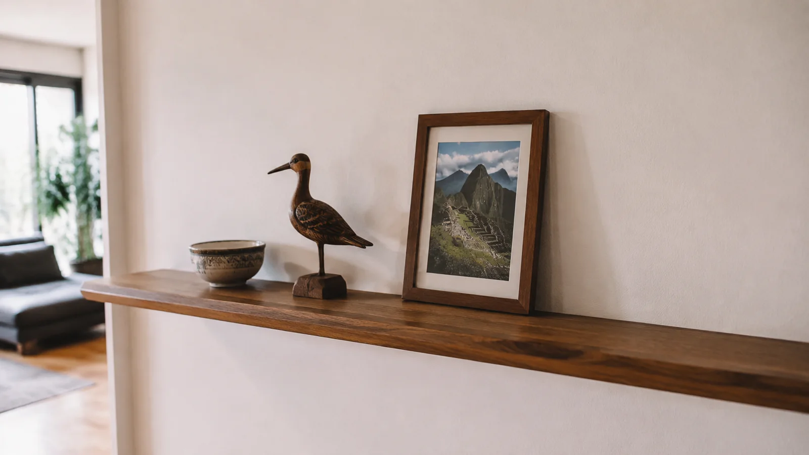 Framed mountain photograph, carved bird, and small bowl displayed on a wooden shelf.