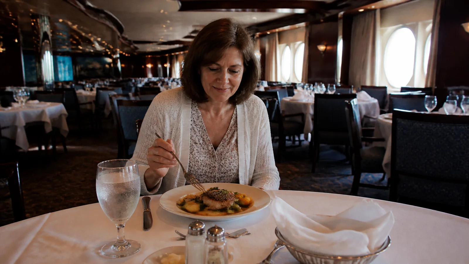 Woman eating dinner alone at a white-clothed table in a ship restaurant.